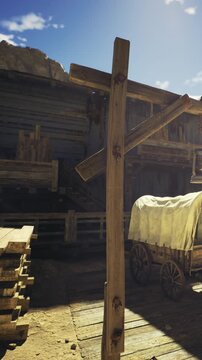 A weathered wooden post reaches upward against a vibrant blue sky. Dusty buildings surround it, hinting at the history of this old western town bathed in warm midday light.