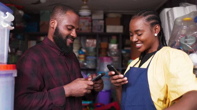 African female entrepreneur processing mobile money payment for a male customer in her store