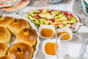 Obraz premium A festive table setting shows round challah bread and sliced apples with honey on the side. There are pomegranate seeds on the apples. This is a part of Rosh Hashanah traditions.