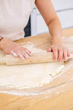 Home cooking. Treat making. Woman baker hand rolling dough sheet with kitchen pin on flour domestic countertop preparing sweet dessert.