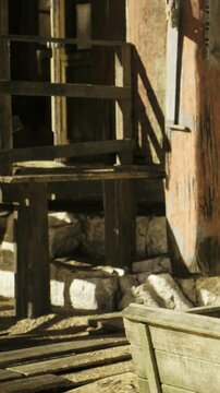 Sunlight dances on the weathered wood of a rustic structure, highlighting its natural beauty. The surrounding stones and shadows create a peaceful atmosphere, inviting curiosity.