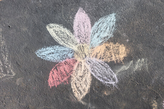 child's drawing of daisy with rainbow petals with concrete chalks on driveway