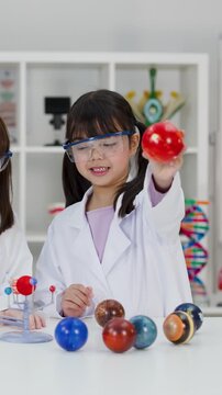 Young Girl in Lab Coat Studying Solar System Model in Classroom