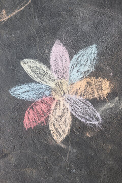child's drawing of daisy with rainbow petals with concrete chalks on driveway