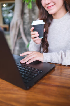 Vertical closeup image of a woman working on laptop computer and drinking coffee in cafe