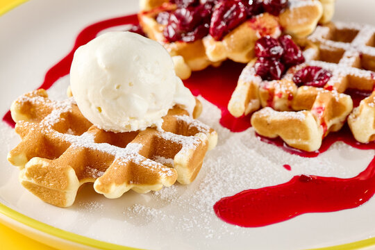 Golden Belgian waffle with creamy ice cream, juicy cherry topping and glossy red sauce for a colorful dessert menu