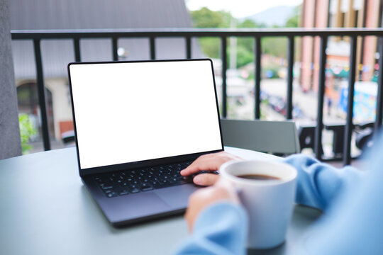 Mockup image of a woman working on laptop computer with blank white desktop screen while drinking coffee in cafe