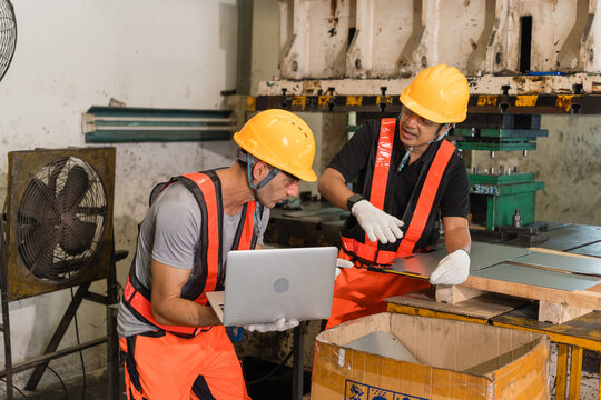 Factory teammate pointing while colleague inspects sheet metal part near punch press highlighting skilled labor and industrial teamwork in the automotive parts manufacturing sector