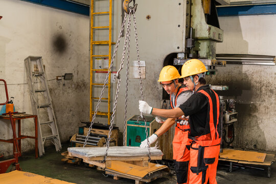 Workers guiding chain-hoisted metal load onto pallet in stamping factory