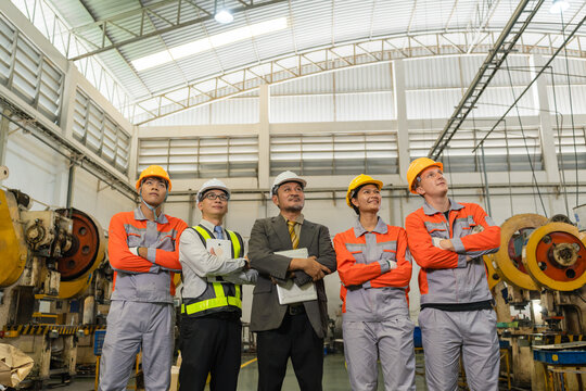 Factory team of manager, engineer and machine operators standing between power presses