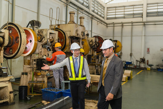 Engineer explaining punch press machinery layout to manager walking through stamping plant