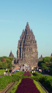 Colorful flower gardens and a symmetrical pathway lead toward the majestic central tower of Prambanan Temple in Indonesia.