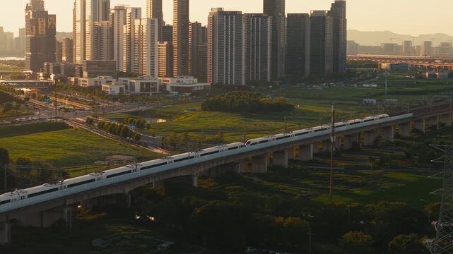 Aerial view of a high speed train travels on an elevated track past tall apartment buildings in a city suburb during sunset in China