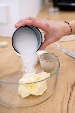 Culinary recipe. Adding sugar. Female chef hand pouring measuring sweet ingredient in glass bowl with white cream butter mass dough.