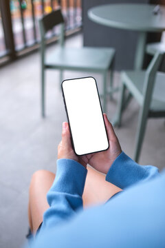 Vertical mockup image of a woman holding and using mobile phone with blank desktop screen in cafe
