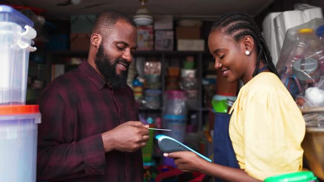 African female shop owner assisting customer with point of sale POS payment and credit card in her shop
