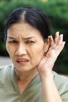 asian senior woman listening with worried expression to bad news on the phone at home, hard of hearing concern