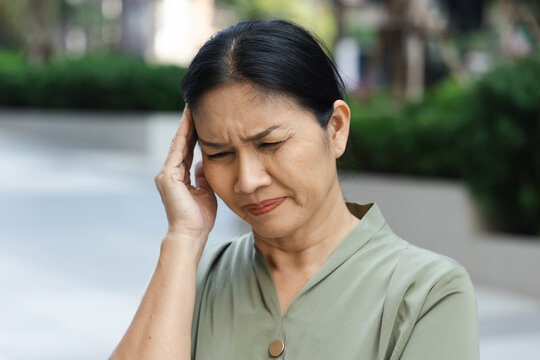 sick asian senior woman suffering from headache on one side of her head, holding temple in pain
