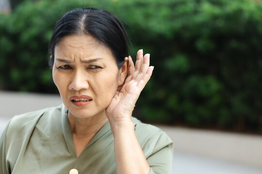 asian senior woman listening with worried expression to bad news on the phone at home, hard of hearing concern