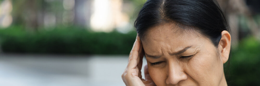 sick asian senior woman suffering from headache on one side of her head, holding temple in pain