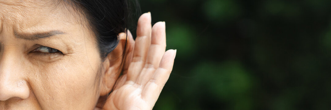 asian senior woman listening with worried expression to bad news on the phone at home, hard of hearing concern