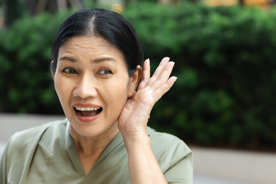 asian aunt, middle aged woman smiling and listening with delight in a green outdoor setting, enjoying positive gossip