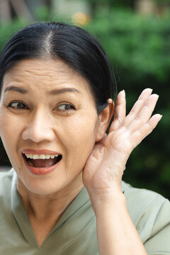 asian aunt, middle aged woman smiling and listening with delight in a green outdoor setting, enjoying positive gossip