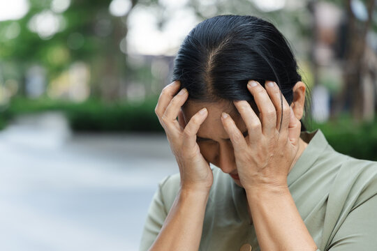 sad asian senior woman doing face palm gesture outdoors in a park, feeling disappointed and overwhelmed