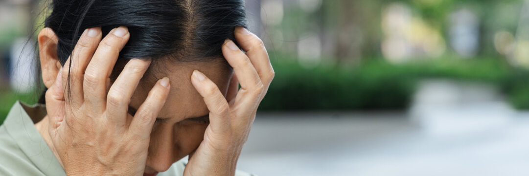 sad asian senior woman doing face palm gesture outdoors in a park, feeling disappointed and overwhelmed