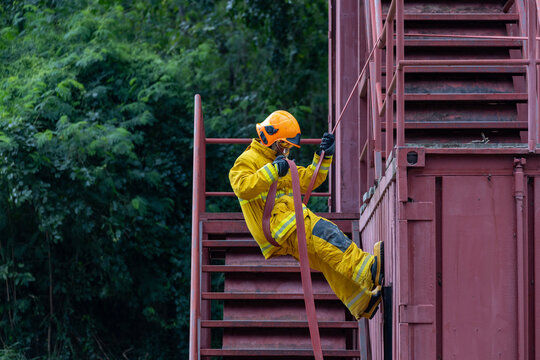 Portrait of firefighter in fireproof clothe rappelling from the burning building full of smoke using rope access for fire extinguish risk rescue mission and accident management
