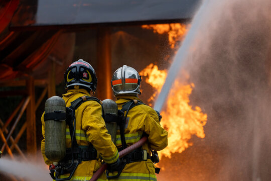 Team of firefighter in fireproof clothes using fog watering hose to put out the burning crashing plane with high flame for fire extinguish risk rescue mission and accident