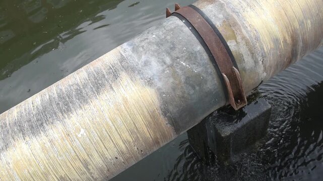water dripping from pipe joint leak, damaged water supply pipeline on supporting concrete base over canal, industrial infrastructure utility decay