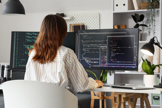 Female software developer coding on multiple computer monitors in a modern office environment, back view, the person is viewed from the back