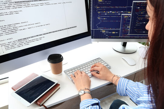 Female programmer coding on a desktop computer with multiple screens displaying complex software development code, the womans hands are actively typing on a keyboard
