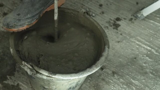 Construction worker mixing cement and mortar with water in a bucket.