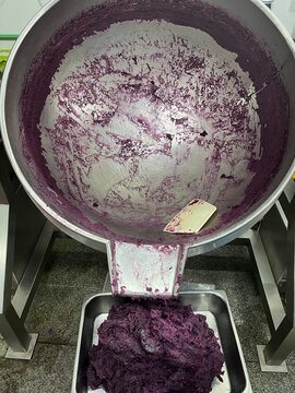 Cooked purple sweet potato filling being discharged from a steam-jacketed kettle into a stainless steel tray after industrial cooking. Food manufacturing process supporting bakery filling production, 