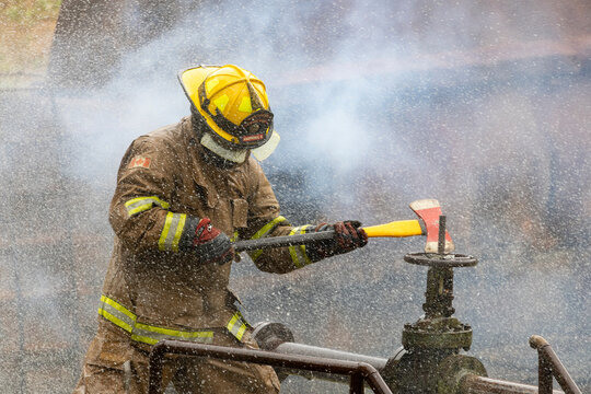 Firefighter in fireproof clothe is holding axe to destroy the water valve near burning building with high flame for fire extinguish risk rescue mission and accident management usage