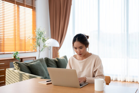 Beautiful young Asian woman working with laptop computer in living room. Work at home