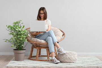 Young woman using laptop in cocoon chair near light wall