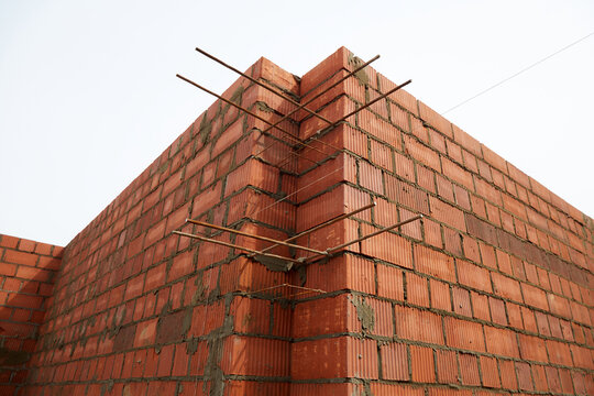 Close-up of a red brick corner wall with exposed reinforcement bars at an unfinished residential construction site