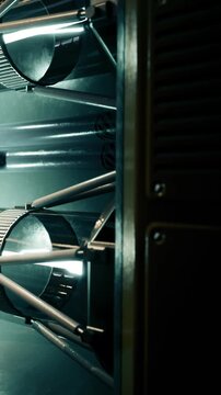 Shiny metallic components of a complex machine reflect dim light in a workshop. Pipes and tubes intertwine, showcasing engineering craftsmanship. A moment captured in a busy industrial setting.