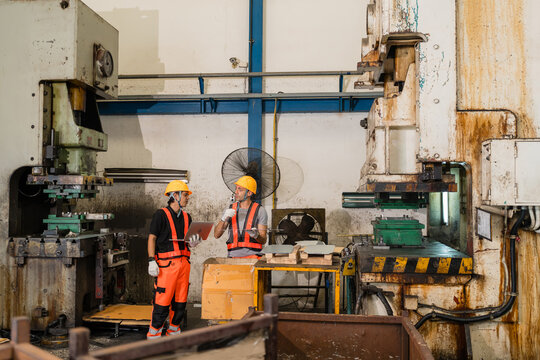 Two factory workers reviewing laptop data between twin power stamping presses in workshop highlighting skilled labor and industrial teamwork in the automotive parts manufacturing sector