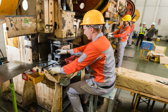 Press machine operator adjusting punch die on power press amid busy metalworking factory floor supporting efficient production and workplace safety inside a busy metalworking factory setting
