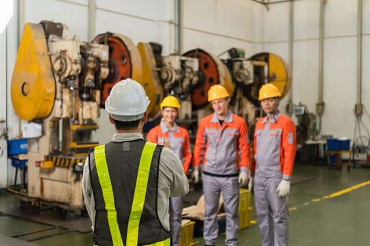 Safety officer photographing three factory workers beside power press machines on shop floor
