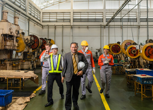 Plant manager leading factory staff past heavy-duty punch press machinery on shop floor ensuring precision and quality in a modern industrial manufacturing environment with heavy machinery