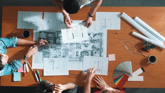Top view of smart architect engineer team talking about project plan while manager walking at meeting table and start working and analyze building construction and looking at blueprint. Symposium.