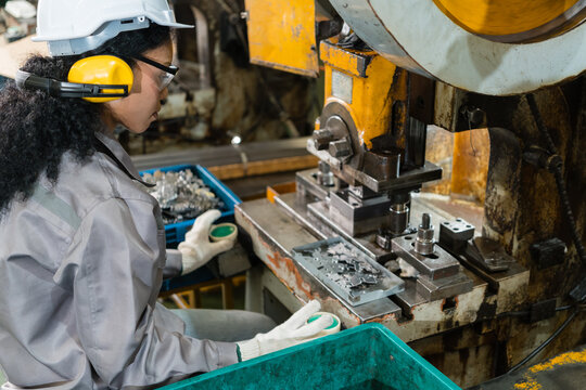 Worker sorting stamped metal parts beside industrial punch press machine supporting efficient production and workplace safety inside a busy metalworking factory setting