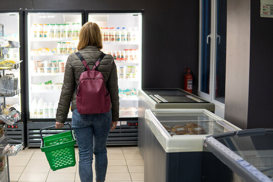 Rear view of woman walking with basket toward dairy refrigerators in grocery store. Concept of household management