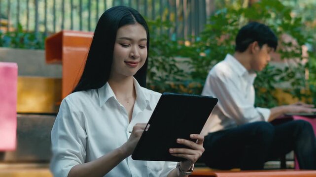 successful asian business woman using phone or digital tablet in front of modern business building.Portrait of businesswoman outdoors.
