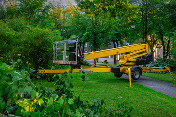 Yellow cherry picker boom lift parked among trees on grass © Oleg
